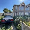 Overgrown garden with parked car beside a semi-detached house under a clear blue sky in a residential neighbourhood