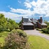 Modern brick house with solar panels surrounded by lush garden and trees under a bright blue sky in the UK countryside