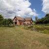 Brick house by a tranquil pond with lush garden under a partly cloudy sky in a countryside setting