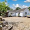 Charming white bungalow with gravel driveway, lush greenery, and a silver car in a sunny countryside setting