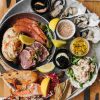 Platter of fresh seafood with prawns, oysters, crab, lemon wedges, and sauces on a round dish atop a wooden table