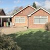 Single-storey red brick house with a well-maintained front garden, under clear blue skies in a suburban setting