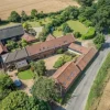 Aerial view of quaint countryside village with red-roofed buildings, lush greenery, and winding road in rural England