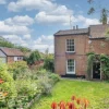 Charming British countryside cottage with lush garden and brick exterior under a blue sky with fluffy clouds