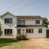 Two-storey suburban house with white facade, pitched roof, garage, and front garden on a sunny day in the UK