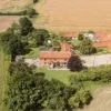 Aerial view of a rural English farmhouse with red roofs surrounded by lush fields and greenery