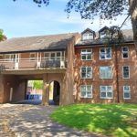 Brick building with arched entrance, surrounded by trees and a lawn, under a clear blue sky