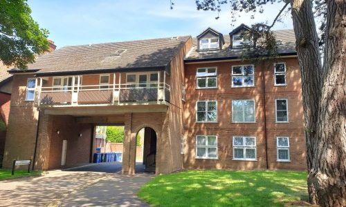 Brick building with arched entrance, surrounded by trees and a lawn, under a clear blue sky