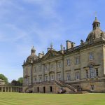 Historic British mansion under a clear blue sky with manicured lawns and classical architecture
