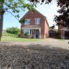 Brick house with blue door, gravel driveway, and tree in front garden on a sunny day in a suburban area