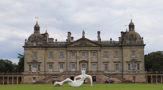 Historic stately home with grand architecture and sculpture on manicured lawn under cloudy sky