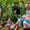 Colourful outdoor scene with a woman in traditional attire, vibrant plants, a panther, tropical birds and dolls on chairs