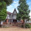 Tudor-style country house surrounded by trees and a garden with clear blue sky