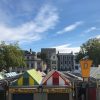 Colourful market stalls with vintage clothing signage under a clear blue sky in a historic city setting