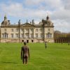 Historic estate with sculptures on a green lawn under a partly cloudy sky in the UK
