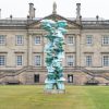 Modern sculpture in front of a historic British mansion, set on a well-manicured green lawn