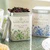 Sandringham Earl Grey and Breakfast Tea tins with floral design on a table with teacups and biscuits