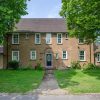 Large brick house with front garden and driveway, surrounded by trees and greenery on a sunny day