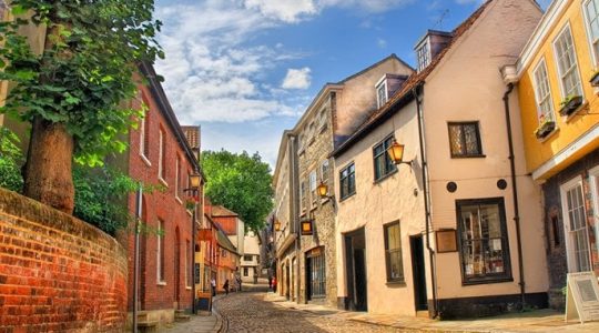 Charming cobblestone street lined with historic buildings under a clear blue sky in a quaint British town