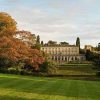 Historic mansion surrounded by lush greenery and autumn trees under a clear sky in the English countryside