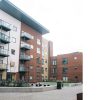 Modern apartment buildings with brick and glass balconies in an urban courtyard setting, featuring landscaped greenery