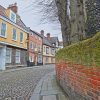 Quaint cobblestone street lined with historic buildings and moss-covered brick wall in a picturesque UK town