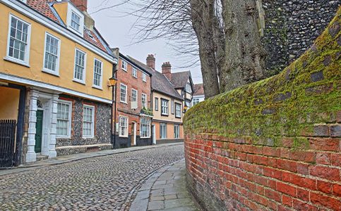 Quaint cobblestone street lined with historic buildings and moss-covered brick wall in a picturesque UK town