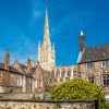 Historic cathedral spire towering above traditional English buildings under a clear blue sky