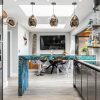 Modern kitchen with sleek cabinets, blue island and pendant lights, large windows opening to a garden view