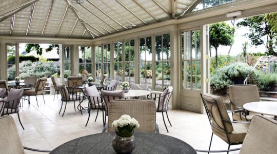 Bright conservatory with elegant seating, surrounded by lush gardens, offering a serene dining experience