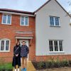 Couple standing outside their newly purchased two-storey red brick and white house in the UK