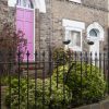 Terraced house with purple door and garden, surrounded by black metal fence in quaint UK neighbourhood