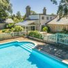 Charming English cottage with glass conservatory and outdoor swimming pool surrounded by lush greenery