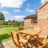 Wooden outdoor dining set on a sunny patio beside a brick house with a lush green garden in the background