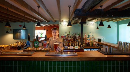 Bartender serving pint in cosy UK pub with wooden beams and well-stocked bar