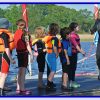 Instructor guiding children in colourful life jackets by a lake for a sailing lesson