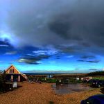 Rural landscape with rustic buildings, vibrant sky, and distant rainbow in the English countryside