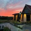Modern house with red brick and wooden accents, set against a vibrant sunset sky in a peaceful rural landscape