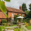 Cosy English pub garden with red brick house, picnic tables, and parasol amidst lush greenery