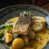 Grilled fish fillet with roasted potatoes, pak choi, and a rich sauce served in a stylish grey dish