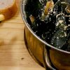Mussels in a metal pot with a side of crispy chips and a slice of fresh bread on a wooden board