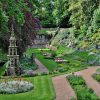Lush English garden with ornate stone structure, vibrant flower beds, and winding paths surrounded by greenery