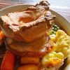 Traditional British roast dinner with Yorkshire pudding, roast beef, potatoes, carrots, peas and gravy on a rustic table