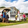 Family enjoying a holiday at a caravan park in summer, unloading car near accommodation under a blue cloudy sky