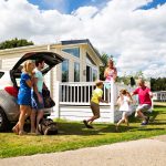 Family enjoying a holiday at a caravan park in summer, unloading car near accommodation under a blue cloudy sky