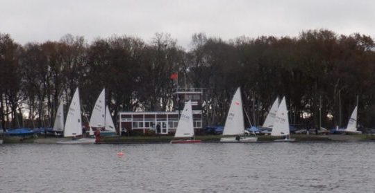 Sailing boats docked by a tree-lined shore on a cloudy day at a scenic lake in the UK