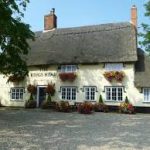 Charming English countryside pub with thatched roof surrounded by colourful flowers and lush greenery
