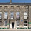 Historic brick building with white framed windows and signs on the ground floor in the UK under a clear blue sky