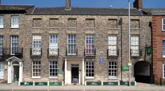 Historic brick building with white framed windows and signs on the ground floor in the UK under a clear blue sky