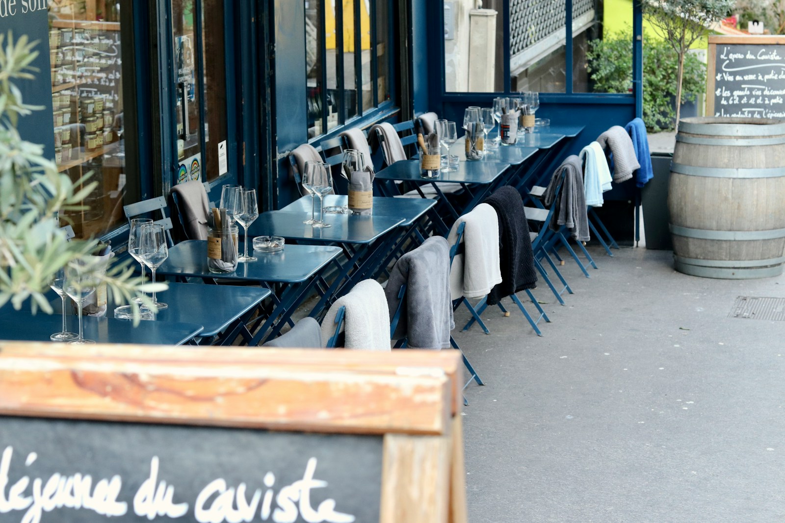 Outdoor café with blue tables and chairs, wine glasses and coats hanging on chair backs, Parisian street atmosphere